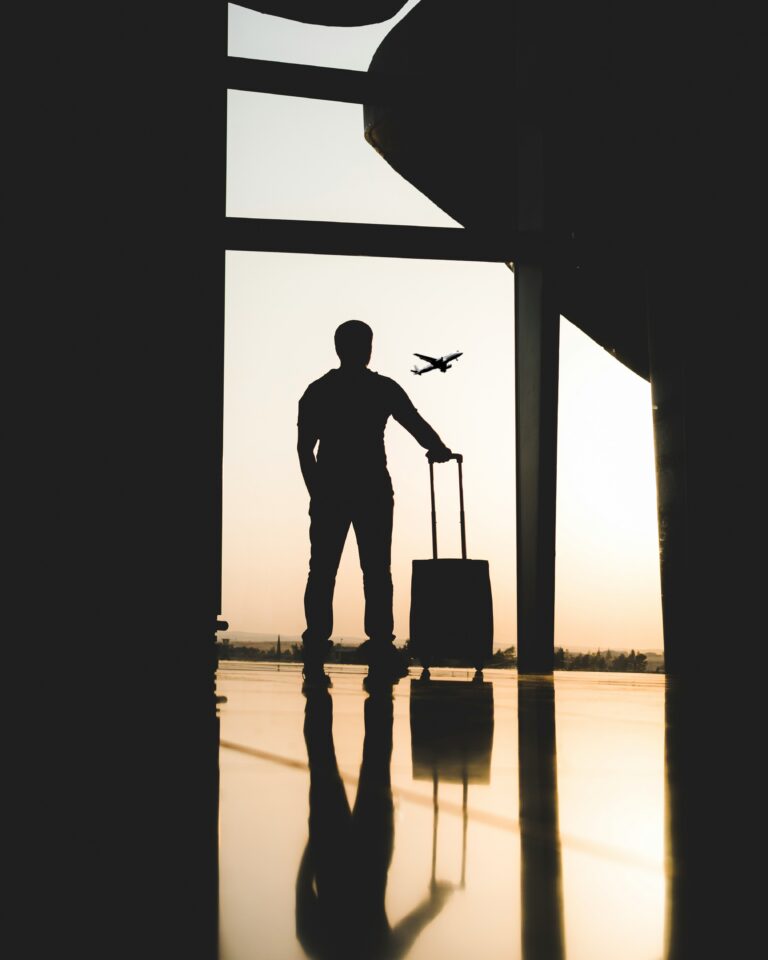 Man with carry on luggage silhouetted at airport terminal