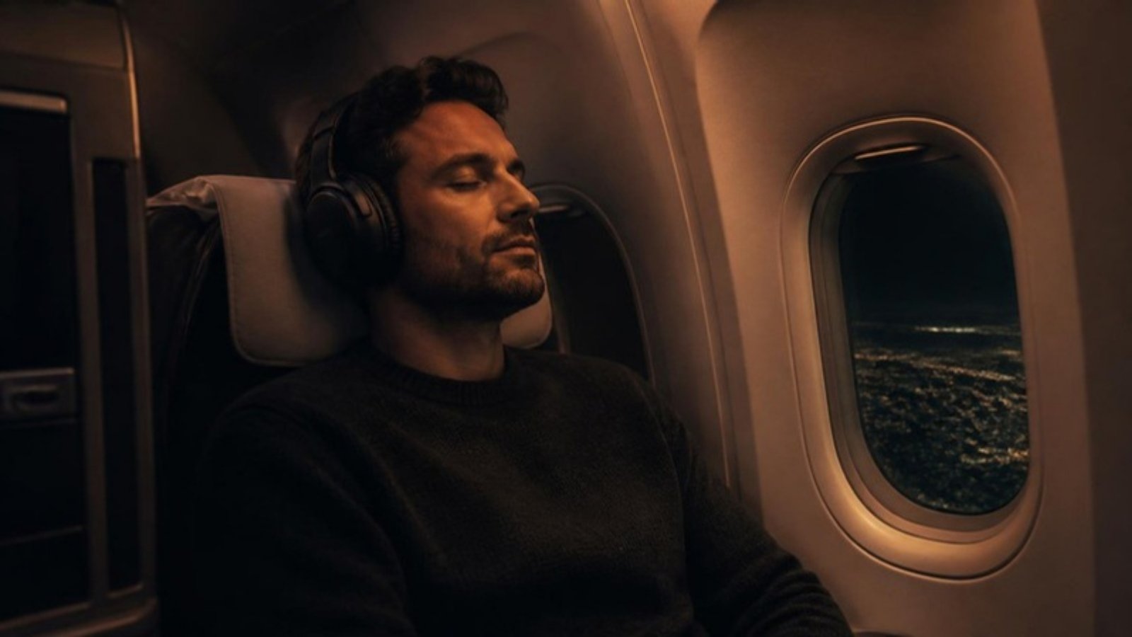 Man wearing noise-canceling headphones in a plane window seat